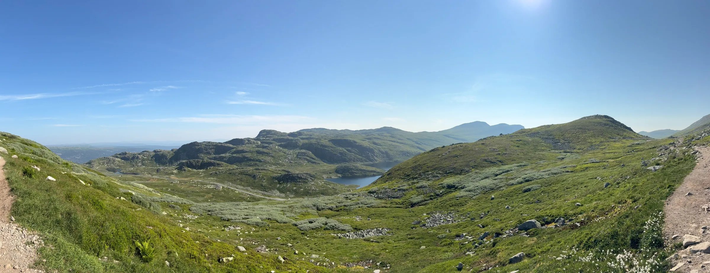 Panorama of a green mountain valley with a lake and a winding road