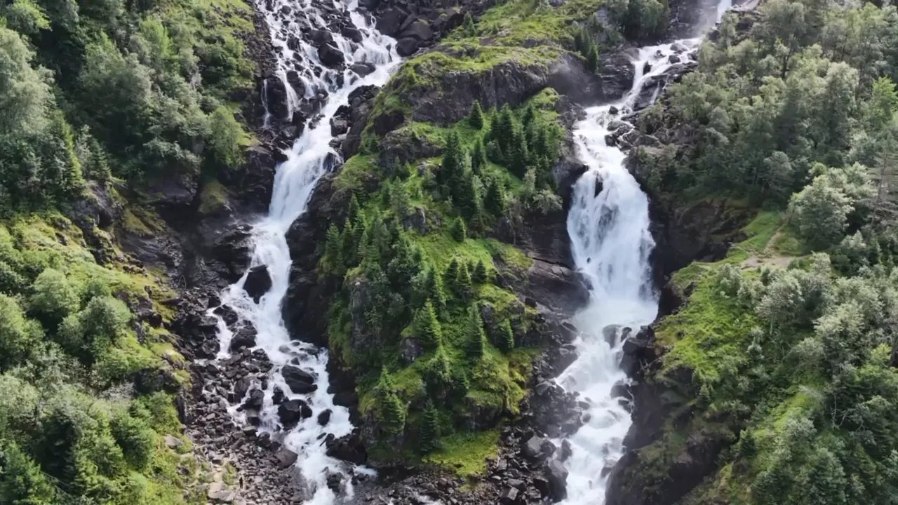 Two waterfalls running down a green gorge, filmed from above