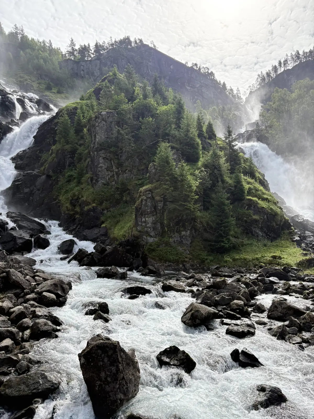 Twee watervallen stromen aan weerszijden van een beboste rots naar een kolkende rivier